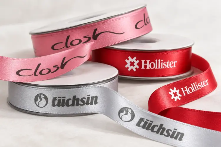 Personalisierte Satinbänder in Rosa, Rot und Silber mit unterschiedlichen Firmenlogos und Aufdrucken