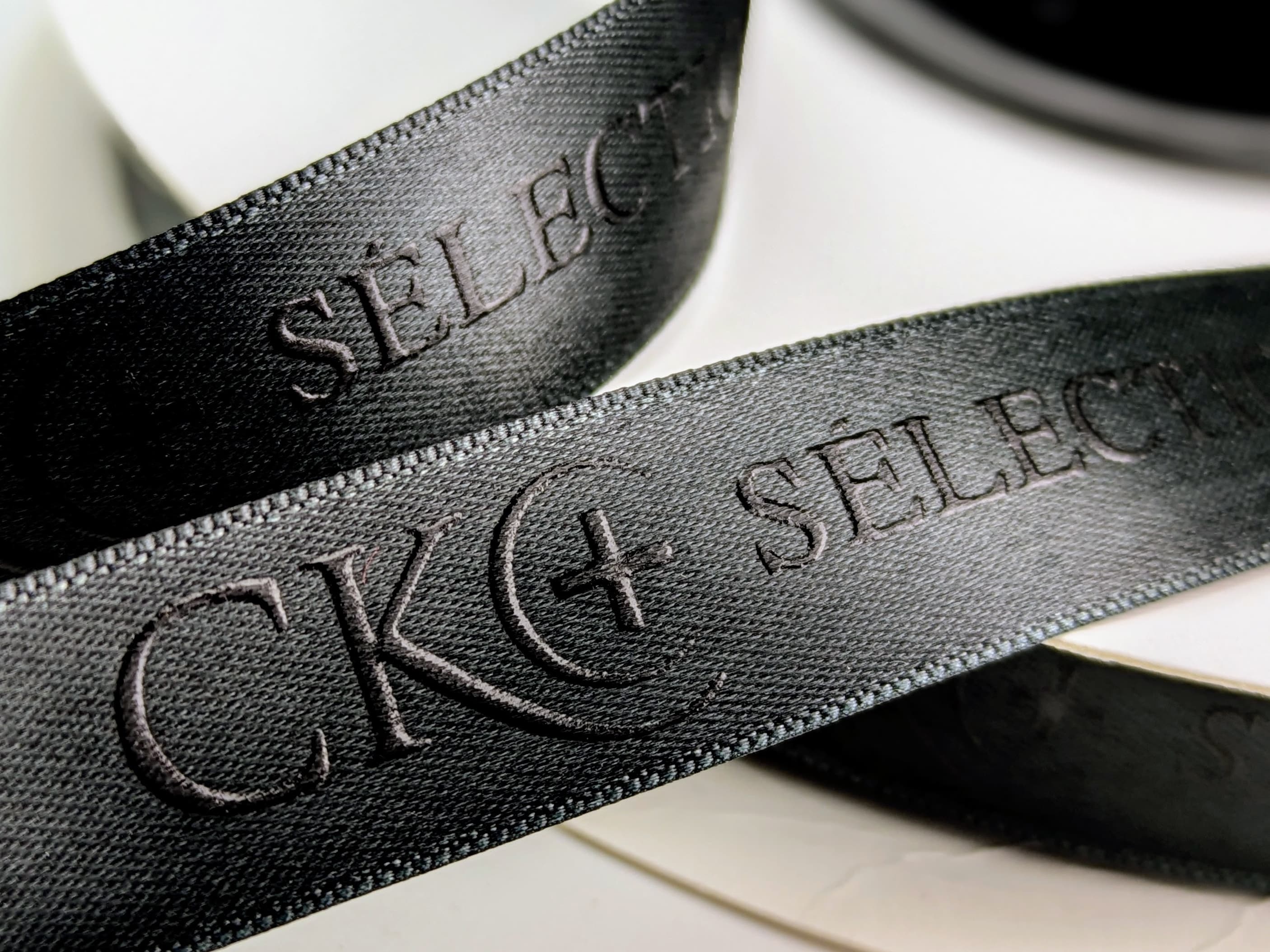 Satinband schwarz mit schwarzem Logodruck als Reliefdruck ausgeführt